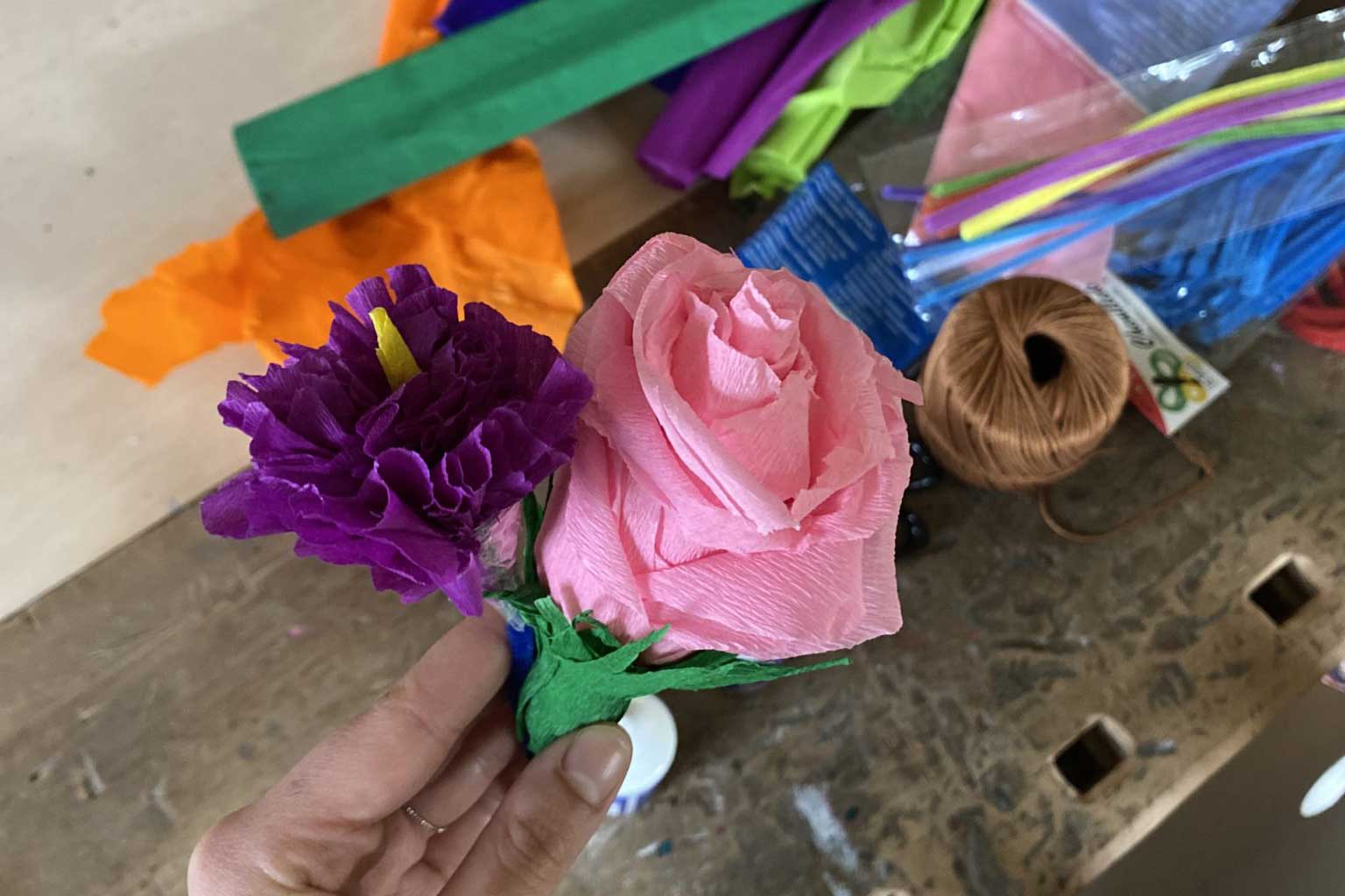 Eine Hand hält eine lila Nelke und rosa Rose auf Papier gemacht