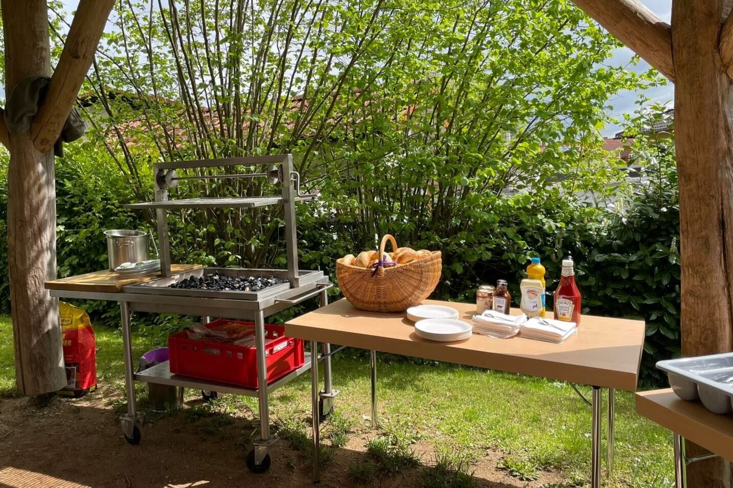 Ein großer Grill ist vorbereitet, Brötchen und Ketchup stehen daneben